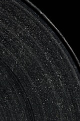 Close-up view of a vinyl record covered in dust and scratch marks, showcasing the grooves and texture of the surface against a dark background.