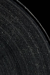 Close-up view of a vinyl record covered in dust and scratch marks, showcasing the grooves and texture of the surface against a dark background.