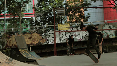 A skateboarder performing a trick on an urban street with graffiti walls.