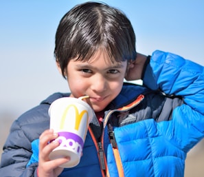 A child smiling while holding a smoothie in a bright, playful setting.