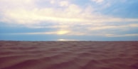 Smooth desert sand dunes under a calm blue sky at sunset.