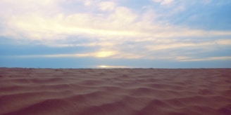 Smooth desert sand dunes under a calm blue sky at sunset.