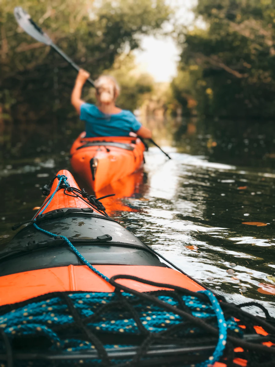 Woman paddling a kayak on calm water while carrying gear for a day trip
