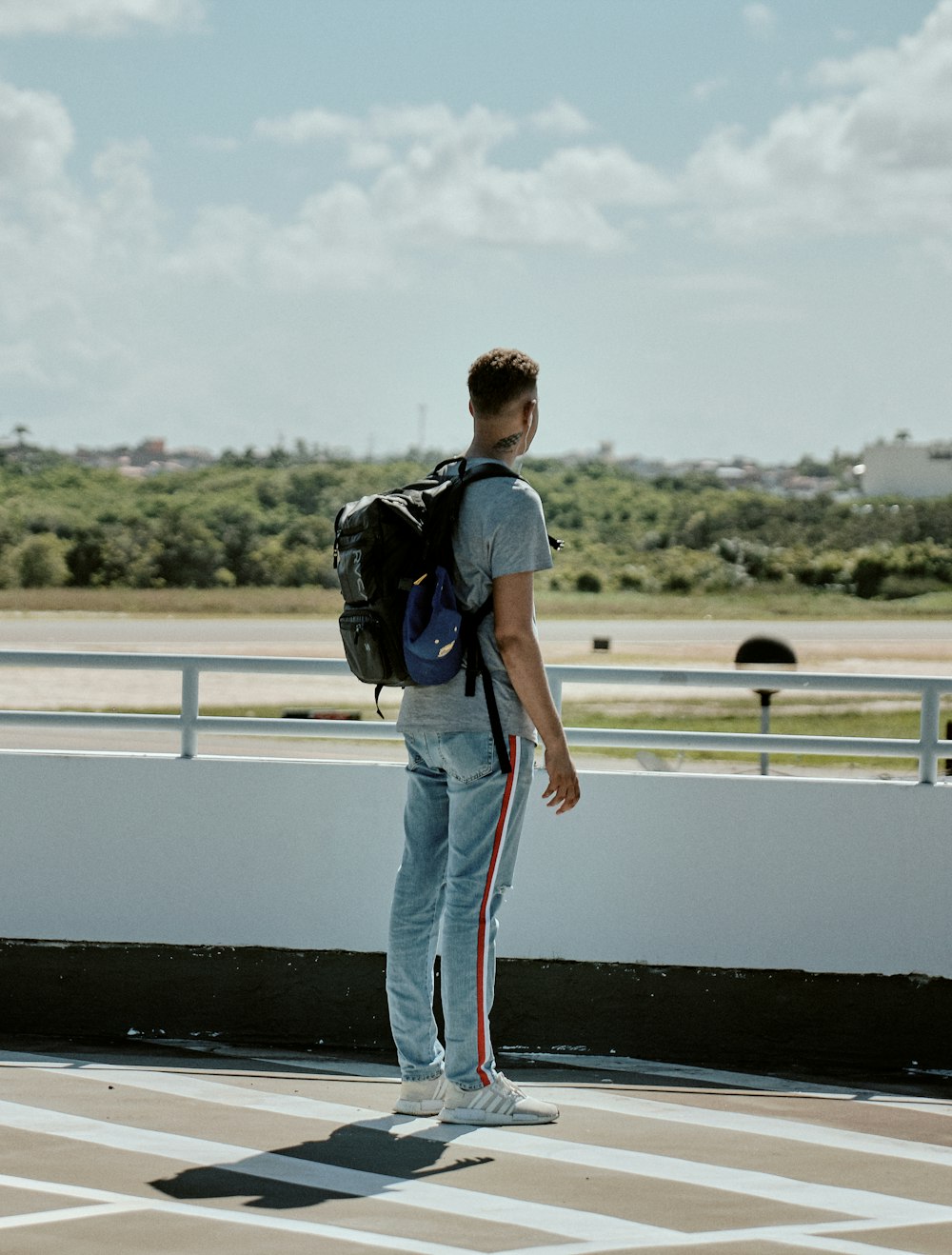 man with black backpack stands facing road