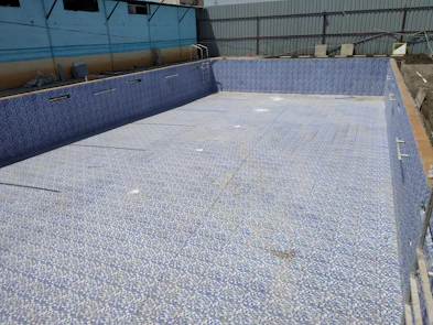 A sleek, modern swimming pool under construction with workers installing tile around the edges.