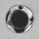 A close-up of a polished, circular metal drain surrounded by a smooth surface, with droplets of water scattered across.