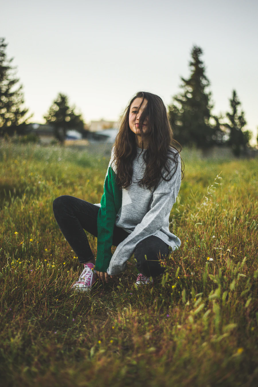 Woman in a colour-block cardigan crouching in a meadow