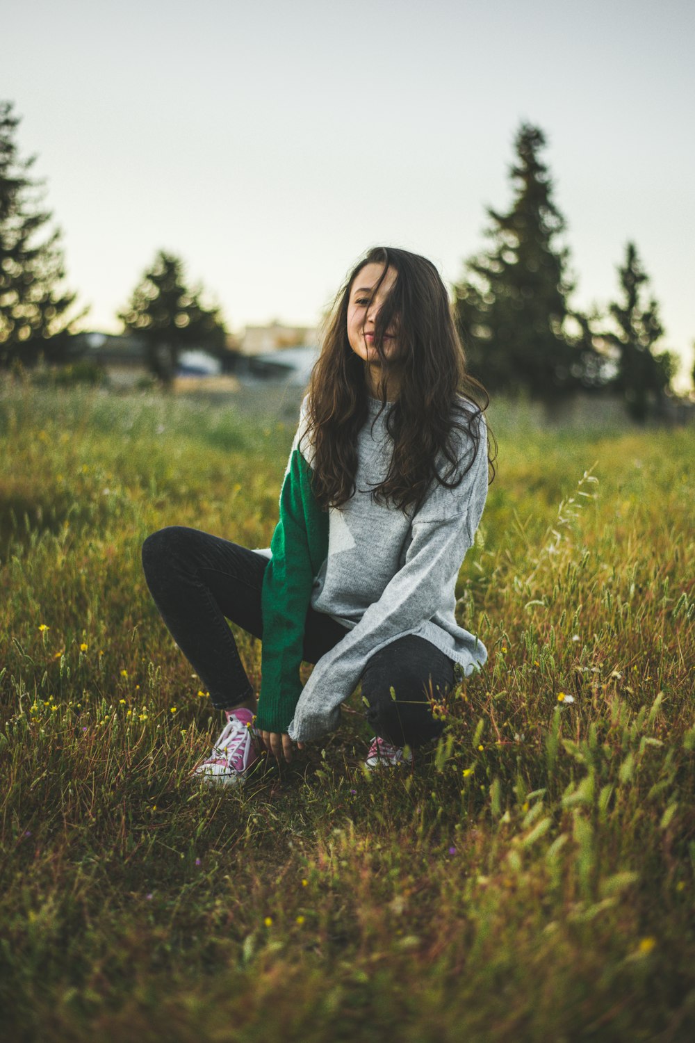 crouching woman wearing gray sweater on green grass field during daytime