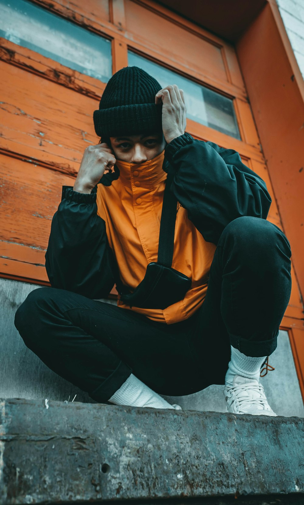 crouching man wearing orange and gray jacket beside wall