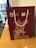 A maroon gift bag with white rope handles. The bag features a detailed drawing of an equestrian statue and logos for the Moscow City Government and Department for External Economic and International Relations. It is placed on a wooden table near a window with buildings visible outside.