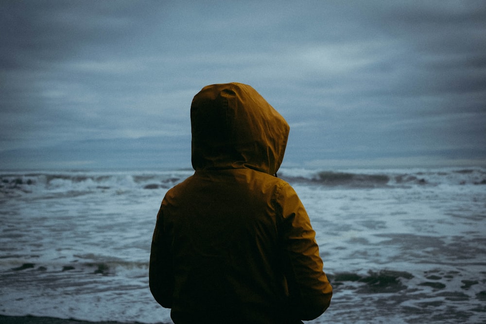 man wearing brown hoodie standing beside seashore