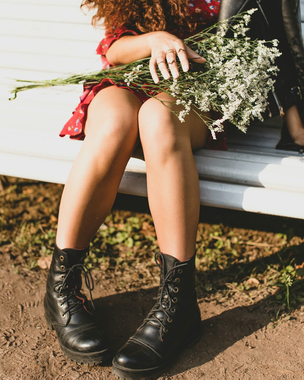 sitting woman in red dress sits on white bench while holding white flower bouquet