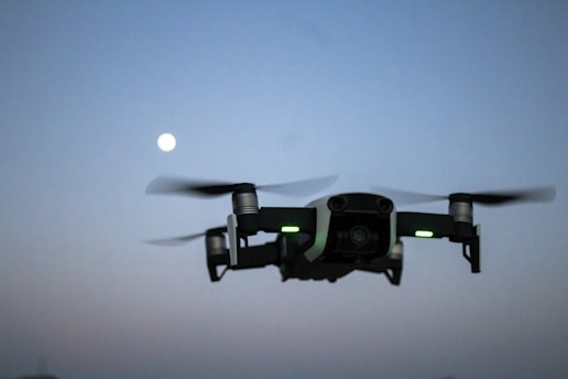 A drone flying over a river border at dusk capturing thermal images for security monitoring.