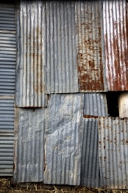 An assortment of corrugated metal sheets, weathered and rusted, are patched together to form a wall. The surface features a mix of textures and hues, with visible signs of aging and corrosion.