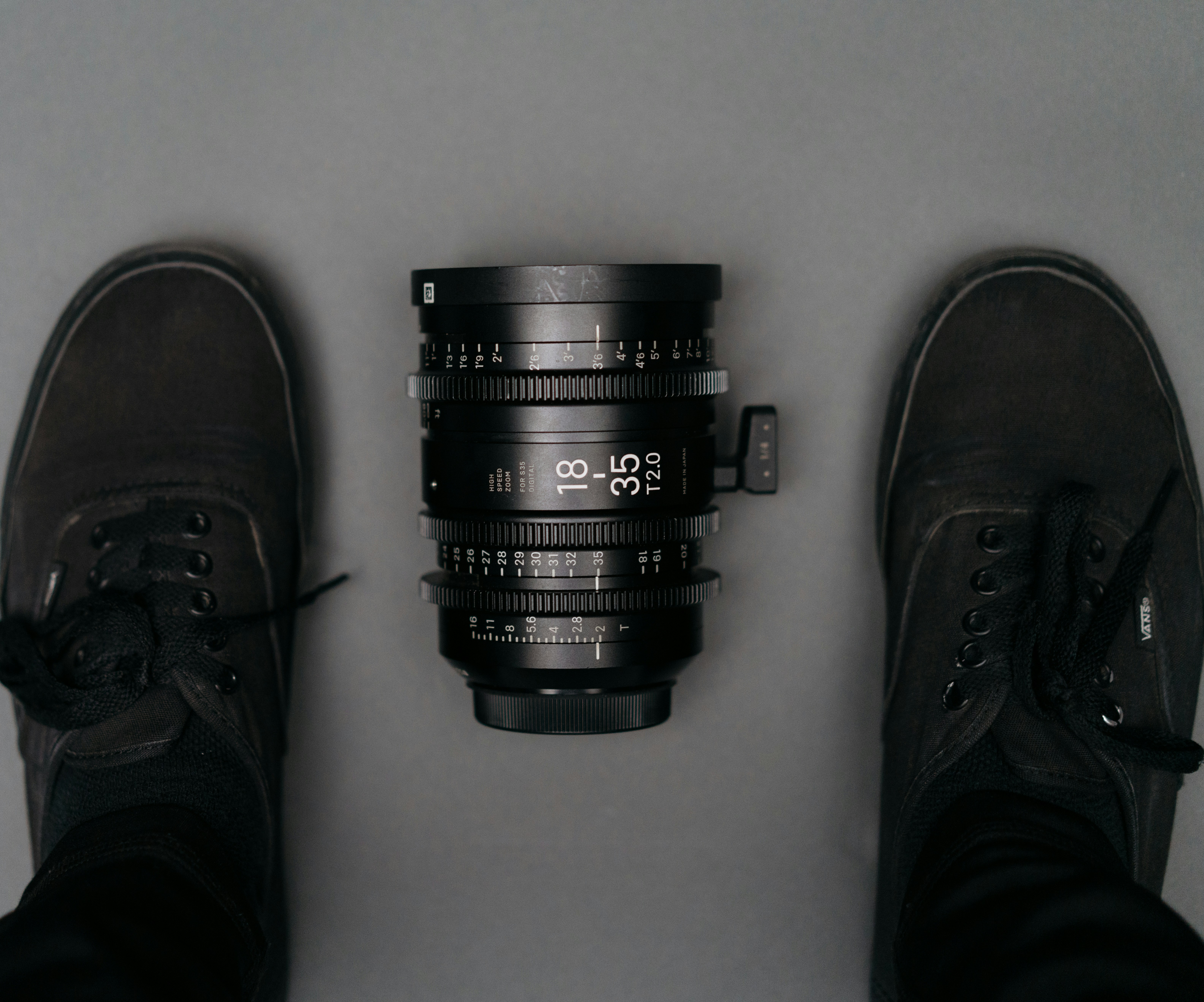 black 18 35 camera zoom lens on floor near person wearing black Vans Authentic sneakers