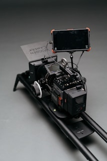 A professional camera rig setup with multiple components, including a large camera, a monitor attached via an arm, and a focus wheel. The setup is mounted on a sliding rail for stabilization and movement.
