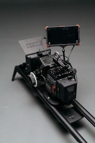 A professional camera rig setup with multiple components, including a large camera, a monitor attached via an arm, and a focus wheel. The setup is mounted on a sliding rail for stabilization and movement.