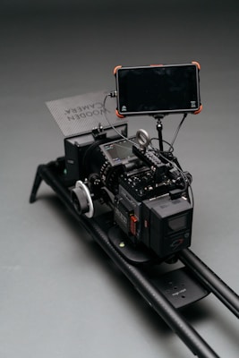 A professional camera rig setup with multiple components, including a large camera, a monitor attached via an arm, and a focus wheel. The setup is mounted on a sliding rail for stabilization and movement.