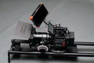 A professional camera setup positioned on a slider. The camera has multiple components including a lens, a follow focus, a matte box with 'Wooden Camera' written on it, and two external monitors.