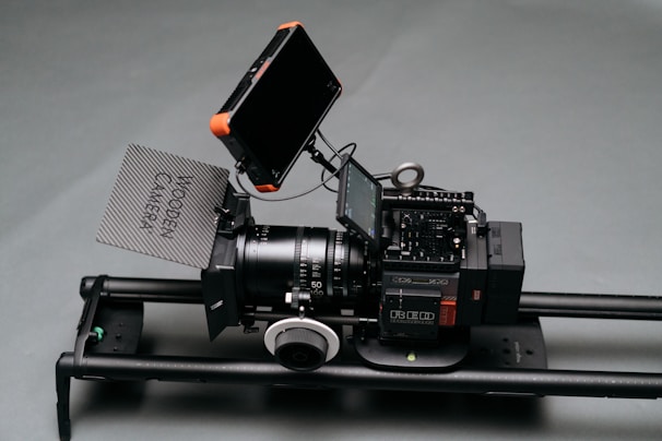 A professional camera setup positioned on a slider. The camera has multiple components including a lens, a follow focus, a matte box with 'Wooden Camera' written on it, and two external monitors.