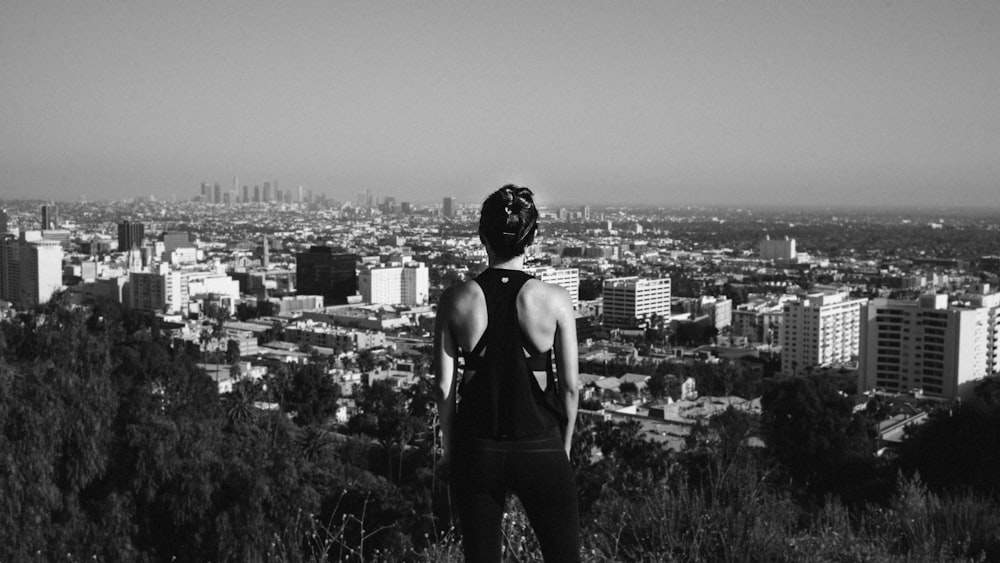 grayscale photography of woman standing near high buildings