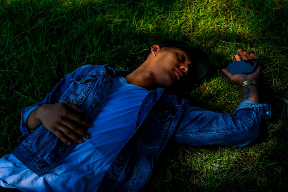 man lying on grass holding smartphone