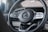 A close-up of a car steering wheel featuring a central logo with surrounding control buttons. The steering wheel is made from a combination of materials including perforated leather and metallic elements.