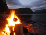 Campfire glowing warmly in a remote canyon surrounded by towering cliffs at dusk.