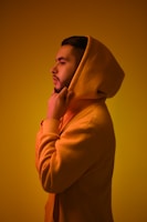 A striking portrait of a model wearing a bold orange hoodie against a dark urban backdrop.
