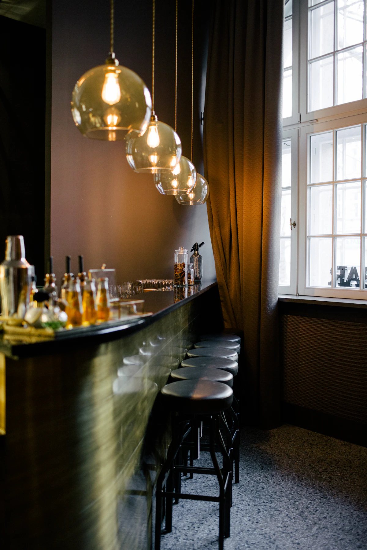 A row of black wooden stools tucked beneath a long bar counter at The Copper Hour.