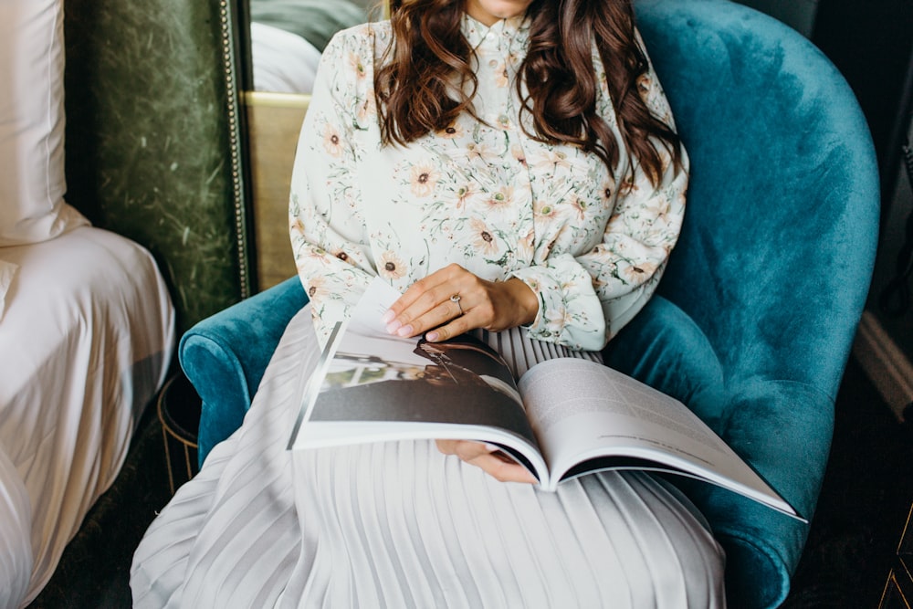 woman reading book sitting on teal sofa chair