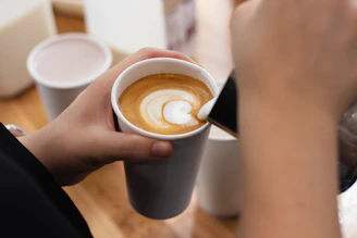 Hands pouring heart-shaped latte art in a cup.