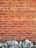 A brick wall with a pattern of horizontal and vertical lines is topped by a row of unevenly shaped, textured stones at the base. The bricks are a reddish-brown color with visible grout lines.