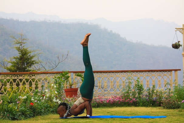 An elegant home garden with a man doing a seated yoga stretch on a light green mat.