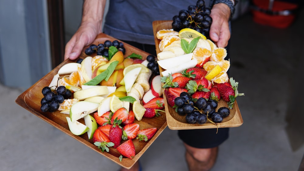 a person holding two trays of fruit