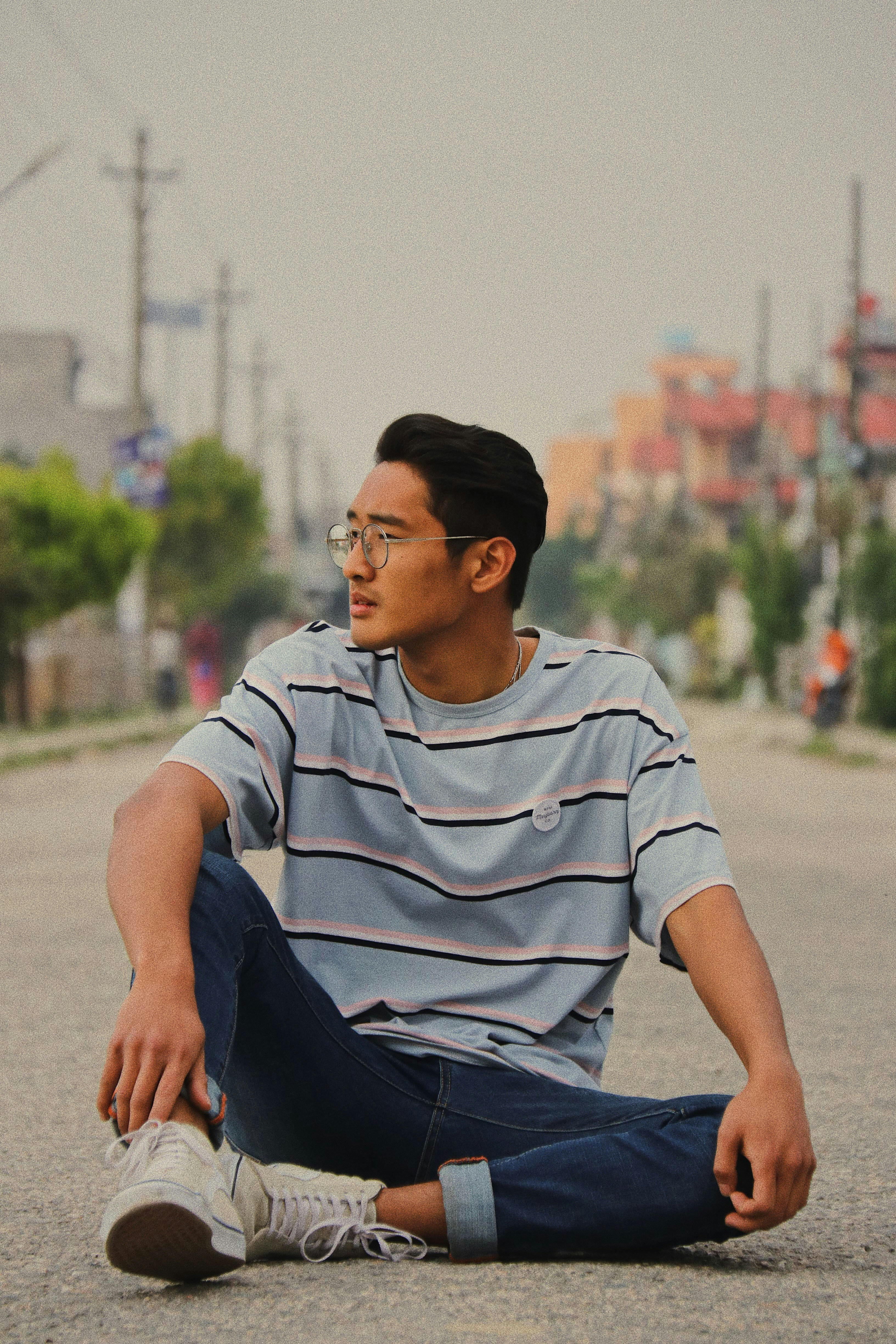 man wearing blue crew-neck shirt and blue denim jean sitting on asphalt road