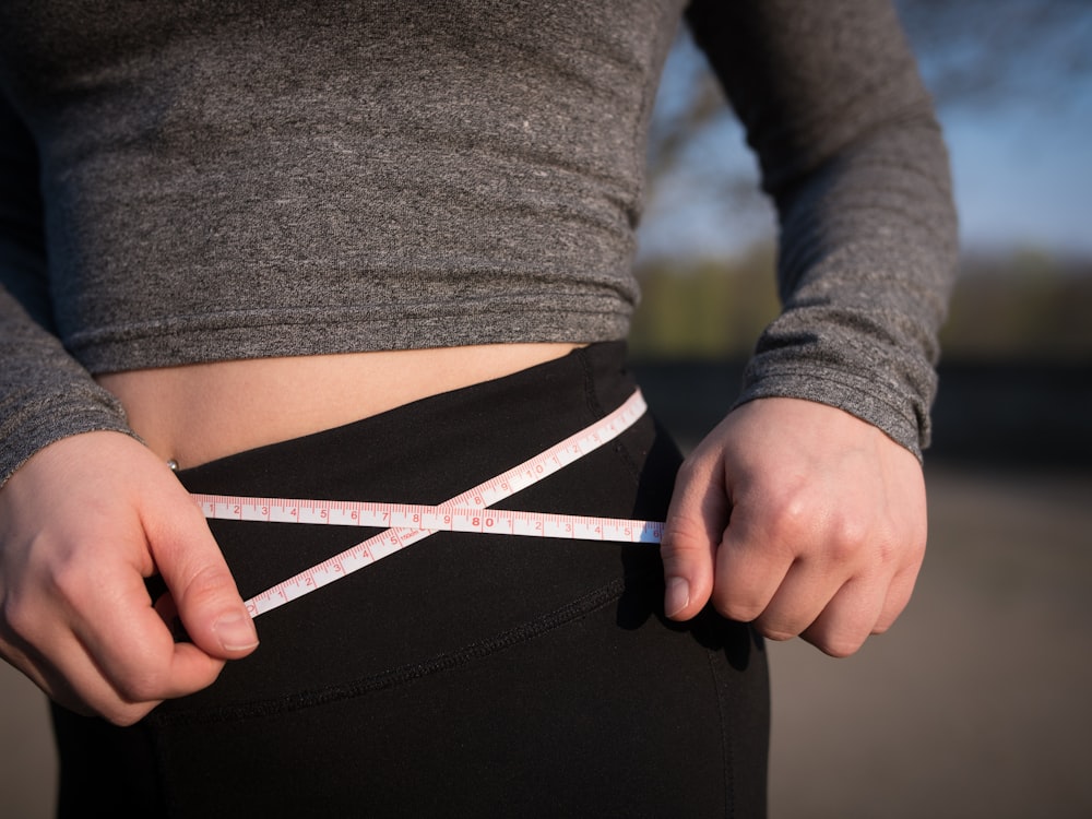 person in gray long-sleeved top and black bottoms measuring waist line