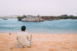man sits on sand dunes while watching the beach