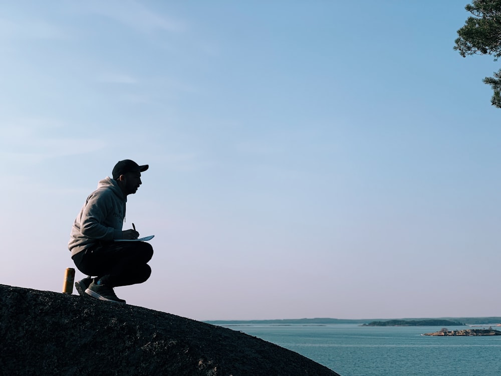 man sitting on hill during daytime near sea