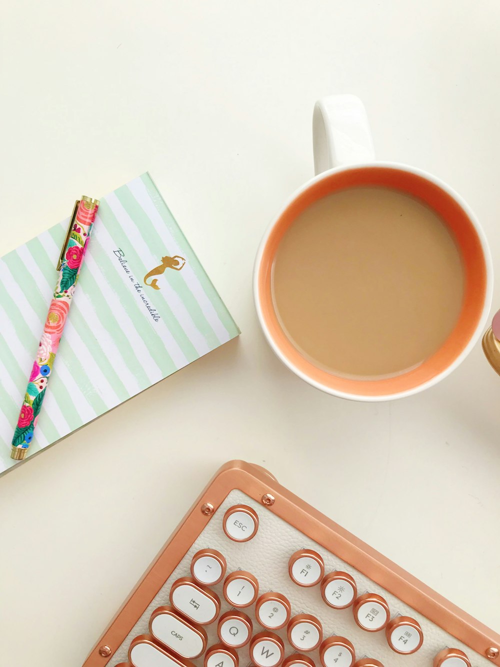 white and orange mug beside pen