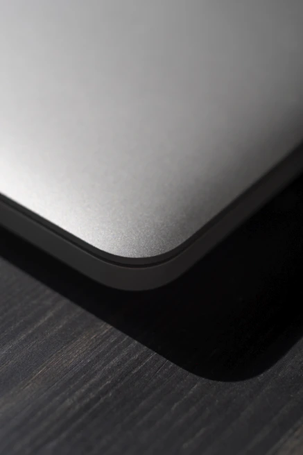 A sleek leather MacBook sleeve resting on a wooden desk with natural light highlighting its texture