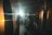In a dimly lit gym, two people are engaged in boxing practice with punching bags. The area is illuminated by bright artificial lights, creating dramatic contrasts between shadows and light. The atmosphere appears intense and focused, with the individuals fully immersed in their workout.
