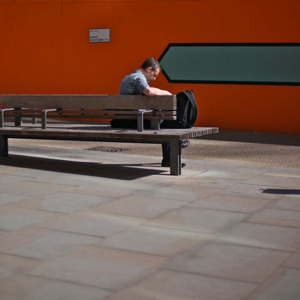 man sits beside backpack on bench