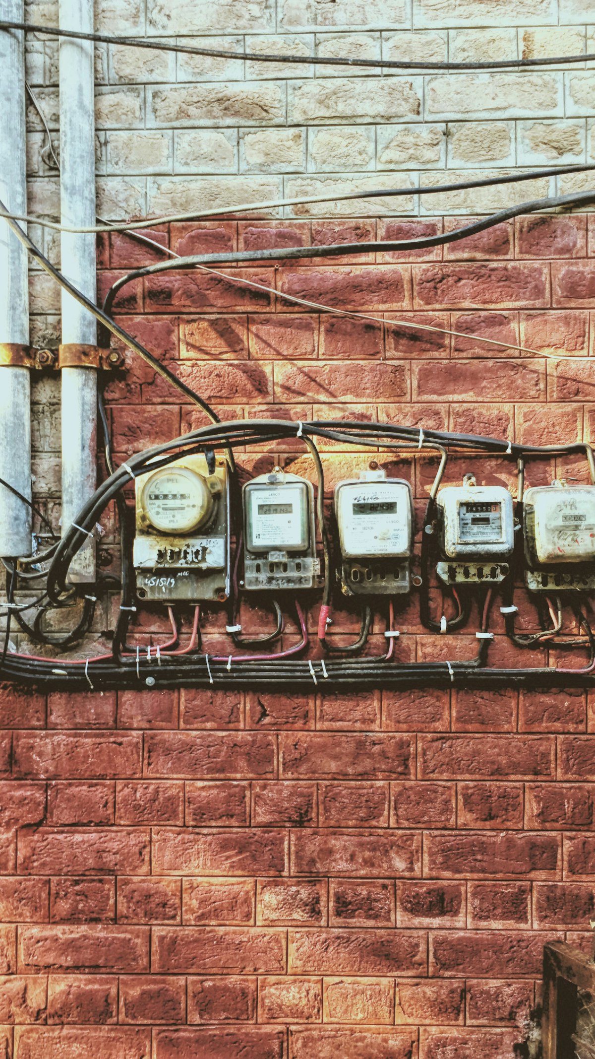 Hilera de cinco medidores eléctricos analógicos montados en una pared de ladrillo con cables