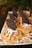 A platter of small tarts topped with caramel, shredded coconut, and half an Oreo cookie. The tarts are arranged in rows on a reflective surface with a blurred green background.