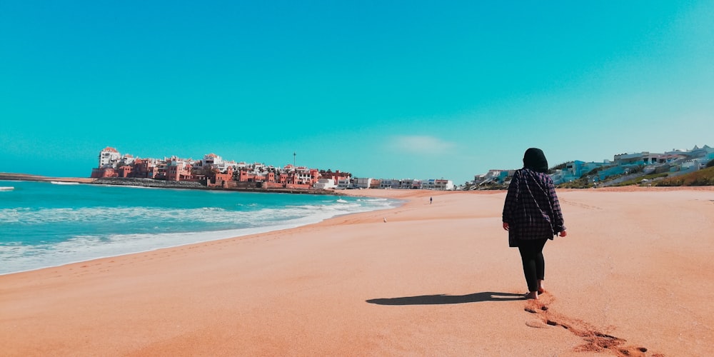 woman wearing black coat walking on seashore