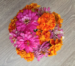 Close-up of a colorful arrangement featuring roses, marigolds, and greenery on a wooden table.