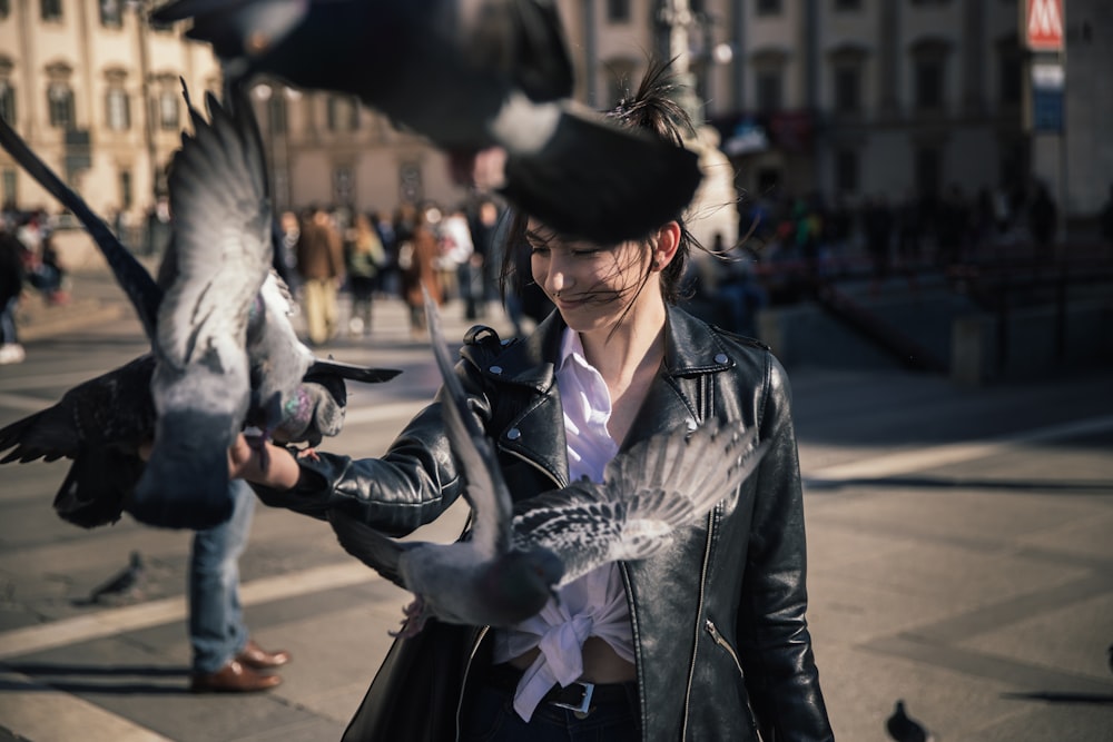 woman wearing black leather jacket holding pigeons