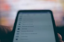 A close-up of a smartphone screen displaying a settings and privacy menu. The text appears slightly blurred, with options like settings, privacy shortcuts, and terms and policies visible. The background is out of focus, creating a contrast with the darker foreground.
