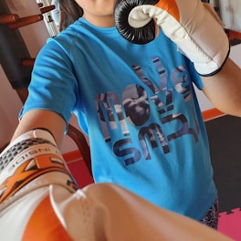 A person wearing a blue t-shirt with the words 'move smart' is holding a black-and-orange punching mitt and wearing boxing gloves. The background shows exercise equipment.